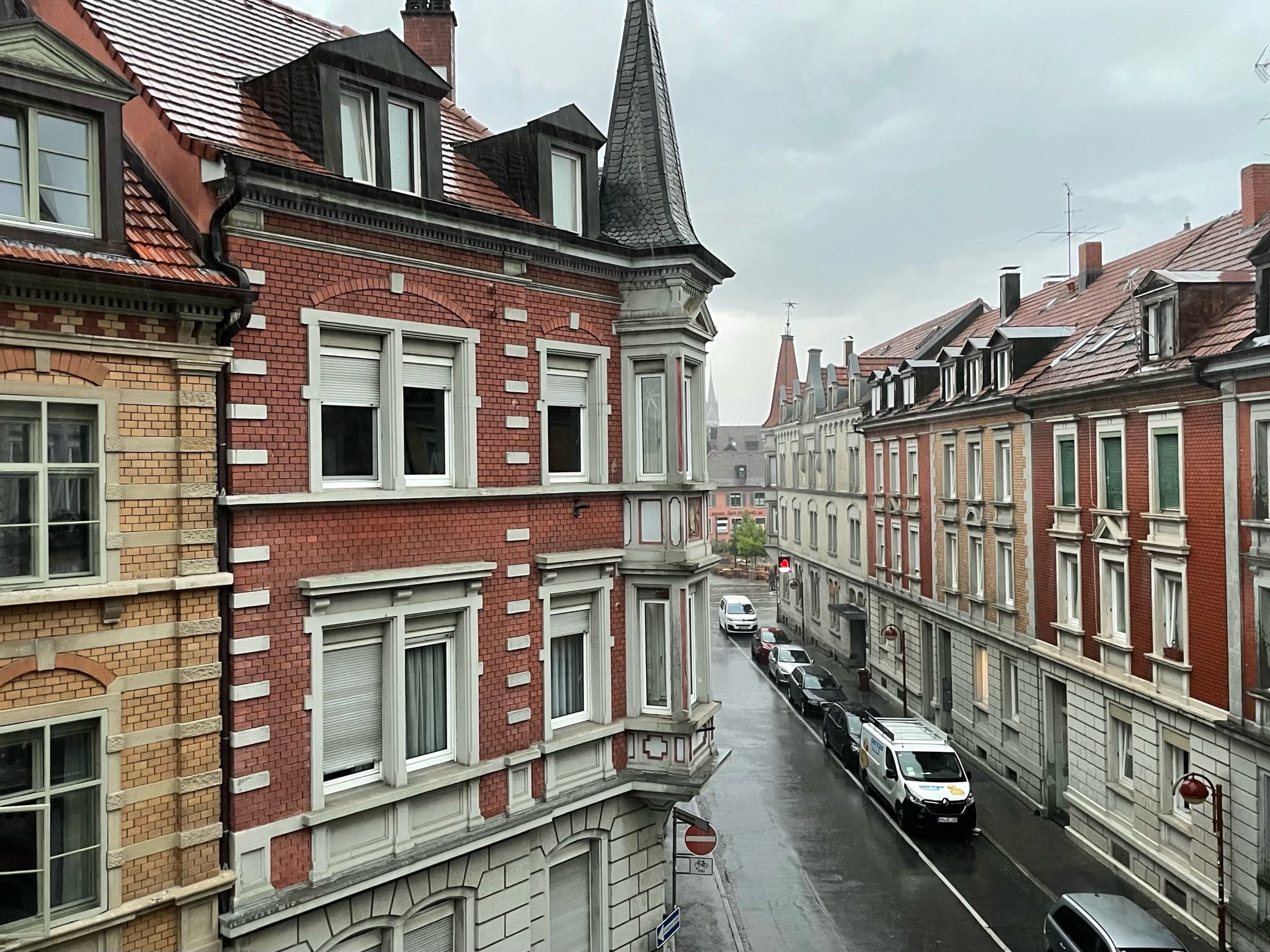 Aussicht aus der oberen Etage auf eine feuchte Stadttraße, sie ist von älteren, dreistöckigen Häusern gesäumt